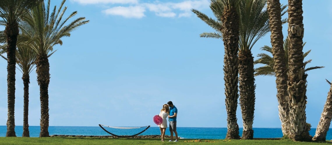 Couple enjoying themselves on the lawn during their holiday in Paphos for adults only at Pioneer Beach Hotel with the sea in the background.