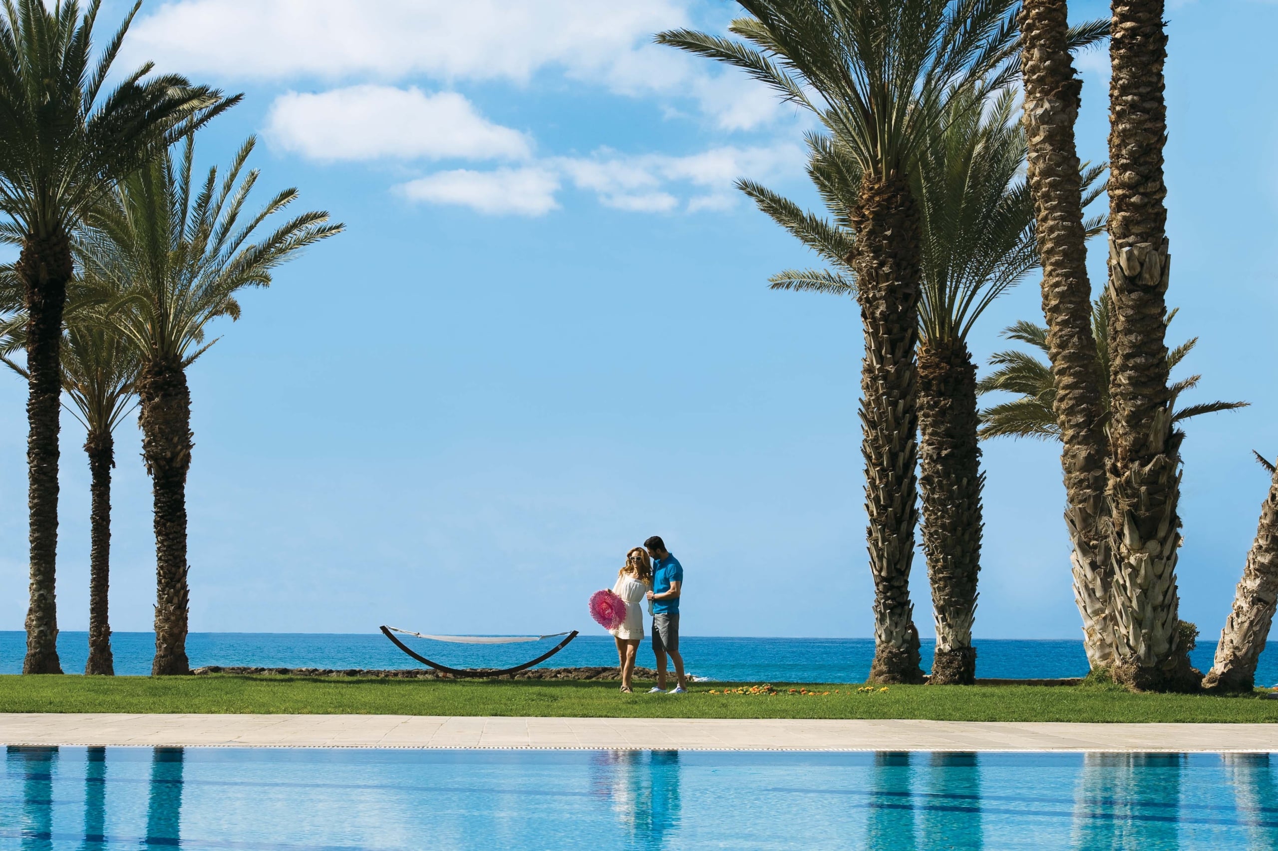 Couple enjoying themselves on the lawn during their holiday in Paphos for adults only at Pioneer Beach Hotel with the sea in the background.